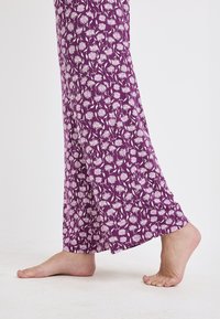 Paarse stoffen broek met witte bloemenprint, losse pasvorm en contrasterende zoomdetails. Zachte textuur, ontworpen voor comfort en bewegingsgemak.