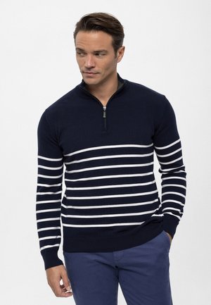 Suéter navy con rayas horizontales blancas, que presenta un collar de media cremallera, puños y dobladillo acanalados. Textura de punto suave, corte ajustado.