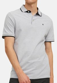 Grijze polo met een donkerdere kraag en mouwafwerking, voorzien van twee knopen en een klein logo op de borst. Gemaakt van gestructureerde stof.
