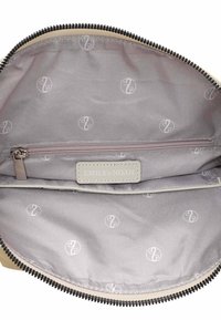 Interior de bolsa beige con un forro de tela gris suave que presenta un sutil patrón de logo. Incluye un bolsillo con cremallera y una etiqueta de cuero de la marca.