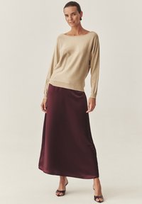 Bež pulover iz pletenine z širokim izrezom, združen z bordo satenasto maxi krilo. Obleka je dopolnjena z odprtimi sandali na peto.