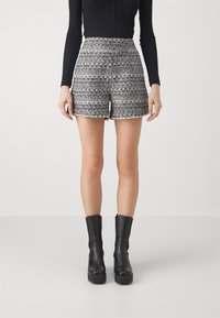 Tweed shorts with a multicolored pattern, frayed hem, high waist, paired with black ankle boots. Smooth texture and tailored fit.