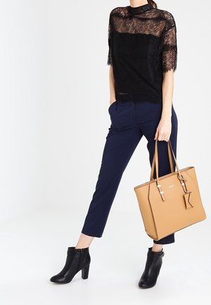 Top in pizzo nero con maniche corte, pantaloni sartoriali blu navy, stivaletti neri e borsa in pelle color cuoio con doppio manico e dettagli argentati.