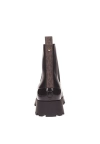 Bottines noires brillantes avec un dos brun à motifs, présentant une semelle épaisse noire et un accent circulaire de marque sur le talon.