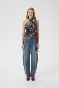 Woman wearing a colorful halter top, wide-leg blue jeans, and burgundy heels, standing against a plain light background.
