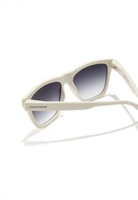 Baltas plastmasas saulesbrilles ar pakāpeniski tumšiem stikliem. Raksturīgas leņķainas rāmji un kājiņas, sānos redzams "HAWKERS" logo. Gluda tekstūra.