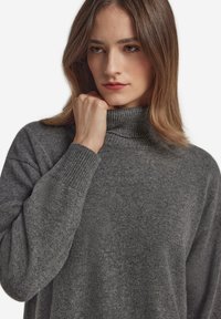 Grauer Rollkragenpullover mit gerippten Bündchen und Kragen, gefertigt aus weichem Strickstoff; zeichnet sich durch eine lockere Passform und eine subtile Textur aus.