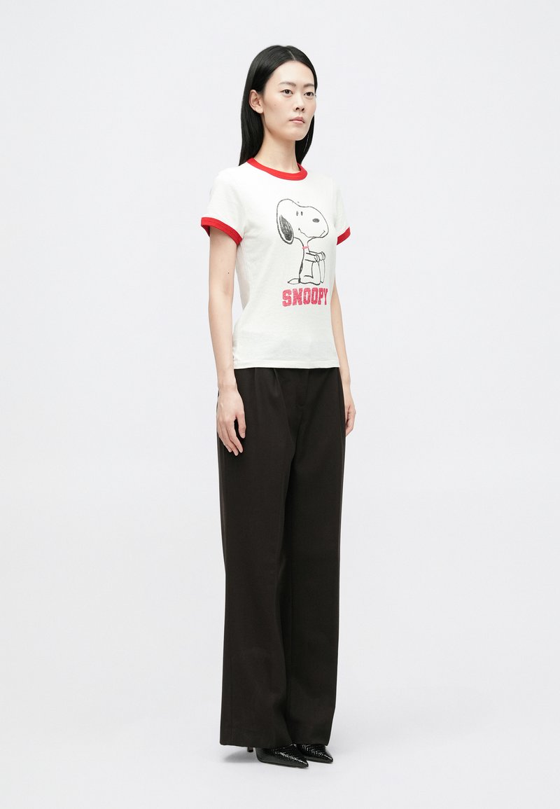 T-shirt blanc avec des manches rouges, présentant un graphique de Snoopy et du texte. Associé à un pantalon large noir taille haute.