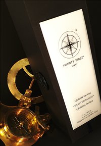 Zwarte verpakking met een wit etiket met tekst en een kompaslogo. Een gouden kompas is gedeeltelijk zichtbaar, met ingewikkelde details en gravures.