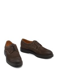 Scarpe in suede marrone con lacci e punta tonda, dettagli in pelle a contrasto e una spessa suola in gomma con pattern di trazione.