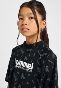 Svart t-shirt med korta Ärmar och hög krage, med ett upprepat logomönster och fet vit text som står "hummel PERFORMANCE" på framsidan.
