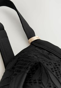 Mustast tekstuuriga kangast kott, milles on kindel rihm ja kulla tooniga metalldetail, millel on keerukad mustrikujundused pinnal.