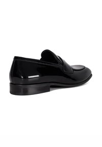 Black patent leather loafer with a rounded toe, low stacked heel, and a stitched design, featuring a distinctive flap over the instep.