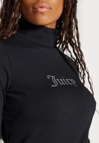 Black turtleneck top made of smooth fabric, featuring crystal embellishment of the word "Juicy" on the front. Close-up view.
