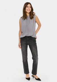 Blusa grigia senza maniche con pieghe sul collo, abbinata a jeans dritti grigi scuri e tacchi a punta neri.
