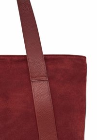 Sac cabas bordeaux avec un corps en suède texturé et une bandoulière en cuir lisse. Le design est simple, avec des lignes épurées et sans accessoires supplémentaires.