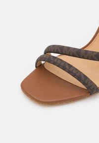 Gros plan d'une sandale marron avec deux brides en tissu foncé à motifs sur un bout carré et une semelle intérieure beige.