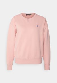 Un sweatshirt rose en coton, avec un col rond, des poignets et un ourlet côtelés, et un petit logo bleu sur la poitrine gauche.
