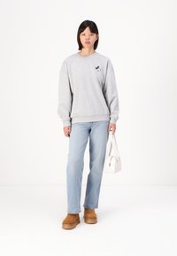 Szürke pulóver, amelyen egy kicsi fekete-fehér Mickey Mouse logó található, világoskék farmernadrággal és világosbarna platform csizmával párosítva. Egy fehér táska van a kezében.