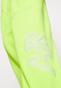 Ljust limegrönt sweatshirtmaterial med texturerad, vit broderad Nike-logga. Har en mjuk, slät textur och en avslappnad passform.