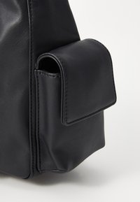 Borsa a tracolla in pelle nera vista di lato, con una finitura testurizzata, una tasca quadrata e cuciture a contrasto lungo i bordi.