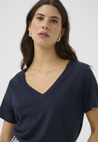 Camiseta de cuello en V de color navy hecha de tela suave, con mangas cortas y un corte relajado, que presenta una textura lisa y mínimos detalles de costura.