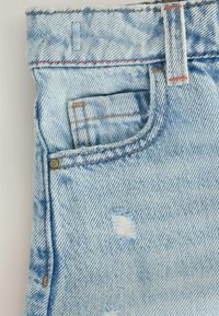 Close-up of light blue denim jeans showing front pocket, small coin pocket, belt loop, and distressed fabric detail.