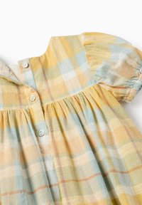 Vestito a quadri giallo e blu con maniche a sbuffo corte, scollatura rotonda e una fila di bottoni. Tessuto leggero con dettagli arricciati.