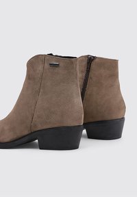 Brown suede ankle boots with a rounded toe, low block heel, and a side zipper. Features a minimal metal accent on the side.