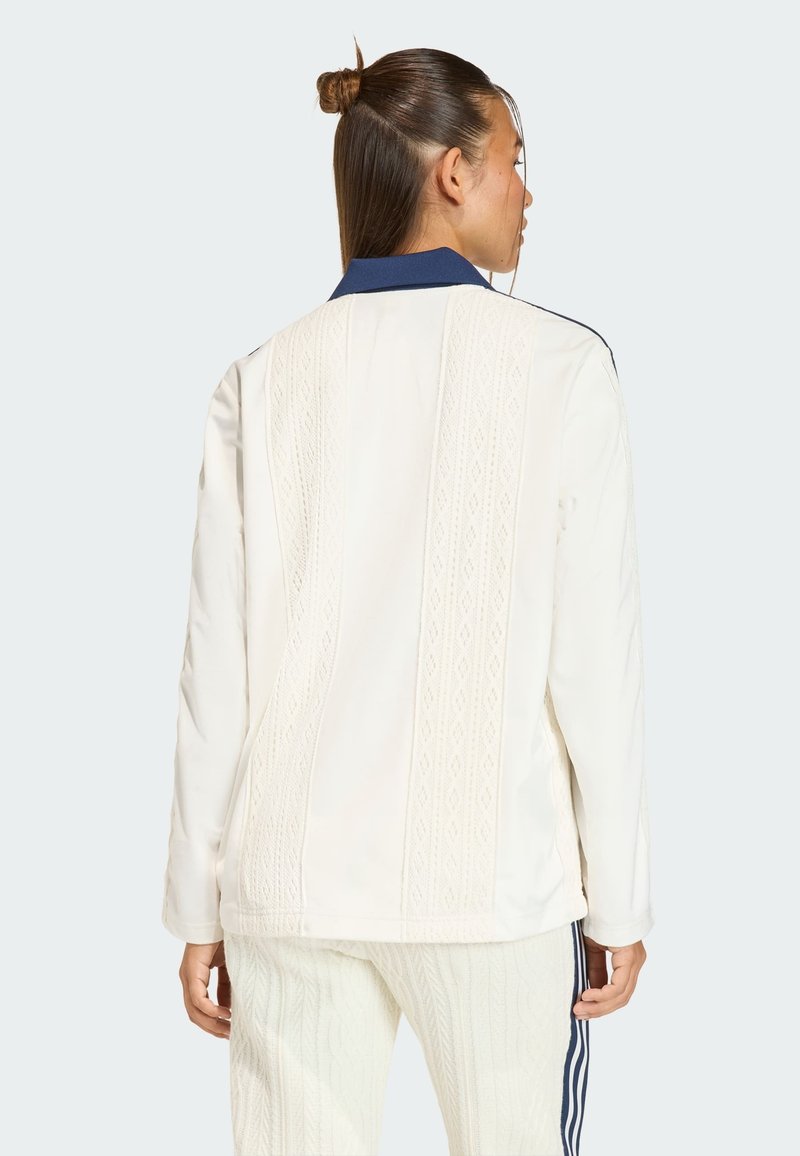 Hvid quiltet jakke med tekstureret lodret mønster, marineblå krave og lange ærmer. Fremhævet med en afslappet pasform, kombineret med cremefarvede bukser.