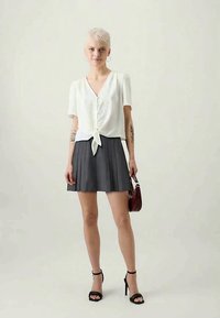 Bela majica s kratkimi rokavi, gumbi in sprednjim zavezovanjem, v kombinaciji z gubano sivo krilo. Obuta v črne pete in drži burgundsko torbico.