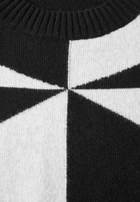 Maglione lavorato a maglia con un motivo geometrico in bianco e nero e colletto a costine. Il tessuto ha una consistenza morbida e blocchi di colore distintivi.