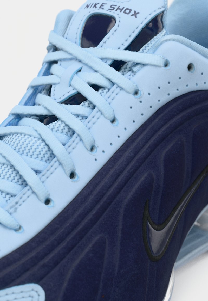 Primer plano de una zapatilla Nike Shox azul que muestra cordones azul claro, parte superior perforada y suela azul oscuro con el logotipo de Nike en negro.