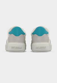 Ζευγάρι λευκών και γκρίζων αθλητικών παπουτσιών με τυρκουάζ ταμπελάκια στη φτέρνα, που φαίνονται από πίσω, με το «LOVE MOSCHINO» χαραγμένο στις σόλες.