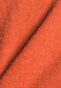 Gros plan sur un tissu orange doux et texturé montrant un motif tricoté et un léger pli.