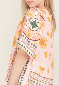 Tunic floreale rosa con motivi gialli e verdi, caratterizzata da un orlo ricamato e una vestibilità rilassata. Maniche corte e scollatura rotonda.