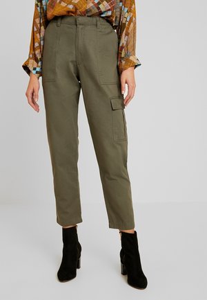 Pantalons cargo vert olive en tissu léger avec jambes fuselées, poches avant et une poche cargo sur le côté. Portés avec des bottes à talons noirs.