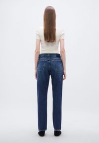 Μπλε τζιν με ψηλή μέση και ίσια γραμμή στα πόδια. Διαθέτουν δύο πίσω τσέπες και μια διακριτική ετικέτα με το λογότυπο στη μέση.