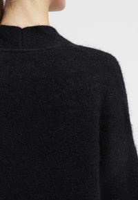Maglione nero in lana caratterizzato da una texture morbida, un taglio rilassato e un collo alto con un piccolo dettaglio a taglio nella parte posteriore.