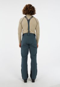 Skibroek in teal met zwarte accenten, voorzien van schouderbanden, een rechte snit en ritsen bij de enkels voor ventilatie.