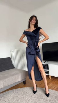 Tengerészkék, vállakat szabadon hagyó ruha texturált anyagból, aszimmetrikus szegéllyel és fodros részletekkel; fekete hegyes orrú magassarkúval párosítva.