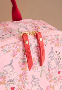 Rózsaszín, virágmintás táska fényes felülettel, piros gumipántos cipzárhúzókkal, aranyszínű fémrészekkel és karakterillusztrációkkal.