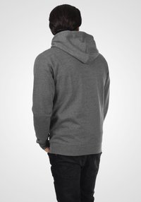 Sweat à capuche gris avec une coupe décontractée, présentant une grande capuche, des poignets côtelés et une texture lisse et douce. Porté avec un jean foncé et ajusté.