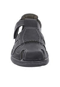 Mustat nahka-sandaalit avoimella muotoilulla, säädettävällä hihnalla, valkoisella ompelulla ja teksturoidulla pohjalla. Yläosassa on leikkauskuvioita.