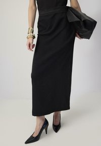 Črna dolga krila iz mehkega materiala, v kombinaciji z visokimi črnimi stiletto petami. Obleka vključuje usklajen pas in usnjeno jakno.