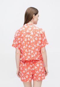 Krótki zestaw z koszulą na guziki i szortami w jasnym koralowym kolorze z białym, kwiatowym wzorem. Krótkie rękawy, luźny krój i gładka faktura.