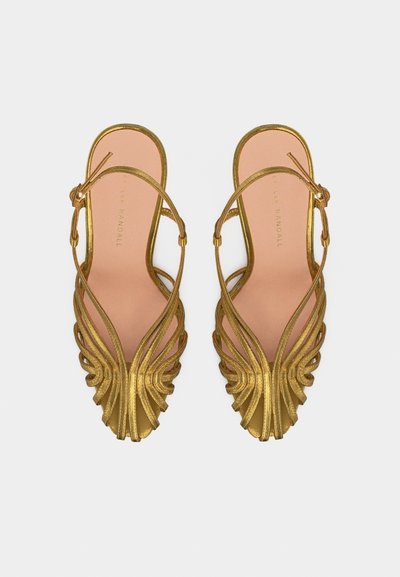 Χρυσά σανδάλια με λουράκια, επίπεδα, με ανοιχτή μύτη και ρυθμιζόμενα λουράκια στον αστράγαλο, εμφανιζόμενα από πάνω σε λευκό φόντο.