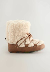Braune Hausschuhe mit weichem, flauschigem Obermaterial in Creme, verziert mit dekorativen Schnürsenkeln und einer strukturierten Gummisohle. Runde Zehenpartie und mittelhohes Design.