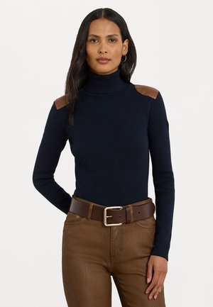 Marineblå turtleneck-genser med ribbestruktur og brune skinnskuldre, kombinert med brune høyt midjede bukser og et matchende belte.