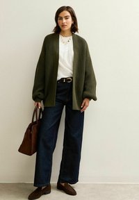 Oliwkowy, ażurowy kardigan, biały bluzka z plisami, ciemnoniebieskie dżinsy o szerokich nogawkach, brązowa torebka i brązowe mokasyny.